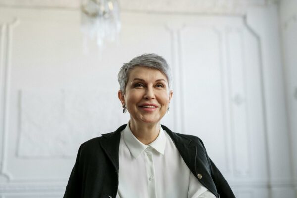 Smiling senior woman in formal attire looking confident in an indoor setting.